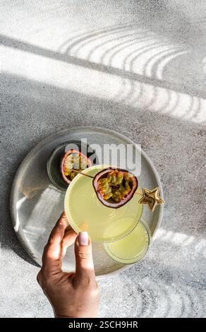 Blick von oben auf eine unbemerkte Person mit einem Glas Gin Tonic Cocktail gemischt mit Passionsfruchtsaft, geschmückt mit einer frischen Passionsfrucht Stockfoto