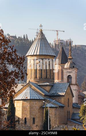 Faszinierender Blick auf die architektonische Landschaft der Innenstadt von Tiflis, die historische Kirchen mit modernen Elementen vor einer ruhigen Kulisse aus Hügeln und Stockfoto