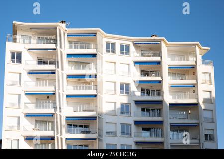 Ein modernes Apartmentgebäude mit blauen Markisen und mehreren Balkonen vor einem klaren blauen Himmel. Die Struktur hebt die Bewohner der Stadt hervor Stockfoto