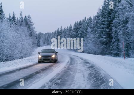 Ein Auto fährt auf einer schneebedeckten Straße, flankiert von dichten, schneebedeckten Bäumen in der ruhigen Landschaft Schwedisch Lapplands, und fängt das Wesen des Winters ein Stockfoto