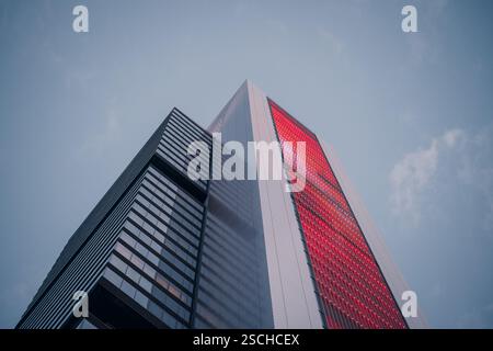 Flacher Blick auf einen modernen Wolkenkratzer mit markanter roter Fassade vor klarem Himmel. Die schlanke Architektur verkörpert urbane Raffinesse und City li Stockfoto
