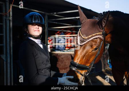 Ein Reiter in formeller Kleidung steht neben einem braunen Pferd, trägt einen Wettkampfschutz und ein Gehörnetz. Die Szene fängt die Eleganz der klassischen Dressur ein Stockfoto
