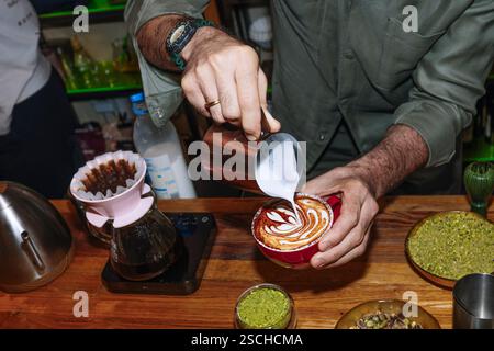Ein Barista kreiert geschickt komplexe Latte Art auf einem frischen Cappuccino. Die Szene verfügt auch über eine Ausgießeinrichtung, die die Kunst der Spezialität betont Stockfoto
