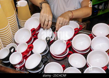 Mit den Händen lassen sich bunte Tassen und Tassen anordnen, die für das Servieren von Kaffeespezialitäten bereit sind. Ein aufgeräumtes Display symbolisiert Zubereitung und Kunstfertigkeit bei der Kaffeezubereitung. Stockfoto