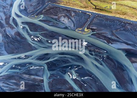 Fesselnde Aussicht aus der Vogelperspektive mit den komplizierten natürlichen Mustern der Flüsse, die sich durch das dunkle Gelände entlang der isländischen Küste schlängeln. Stockfoto