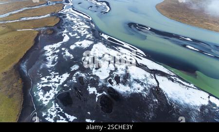 Atemberaubendes Luftdrohnenbild, das Islands Flüsse einfängt, die sich durch schneebedeckte Landschaften in der Nähe der Küste schlängeln und Kontraste von eisblauem Wasser zeigt Stockfoto