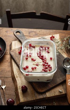 Blick von oben auf reichhaltiges und cremiges hausgemachtes Eis garniert mit roten Johannisbeeren und Stachelbeeren in einem Glasgericht, ausgestellt auf einem rustikalen Holztisch mit u Stockfoto