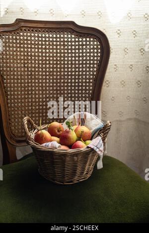 Ein Korb mit Birnen steht auf einem Vintage-Stuhl. Die Szene strahlt rustikalen Charme aus, mit komplizierten Details aus gewebten Textilien und Holzfächern Stockfoto