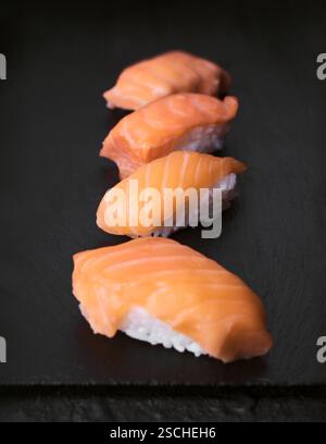 Eine Auswahl an Sushi-Stücken mit Lachs, elegant auf einer schwarzen Steinoberfläche. Perfekt für die Illustration authentischer japanischer Küche und Cu Stockfoto