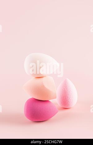 Fein ausbalancierter Stapel lebendiger Make-up-Schwämme mit verschiedenen Formen und Farben in Rosa und weiß vor einem beruhigenden rosa Hintergrund Stockfoto