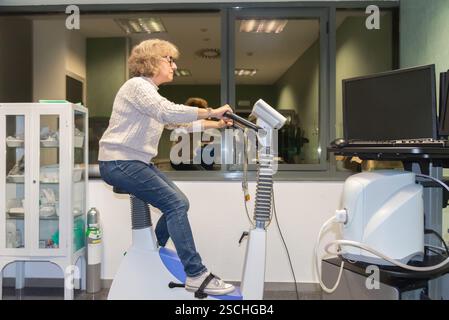 Eine reife Frau nimmt aktiv an einem kardiovaskulären Belastungstest in einer medizinischen Einrichtung Teil und betreibt im Rahmen ihrer Gesundheitsprüfungen ein Heimtrainer Stockfoto