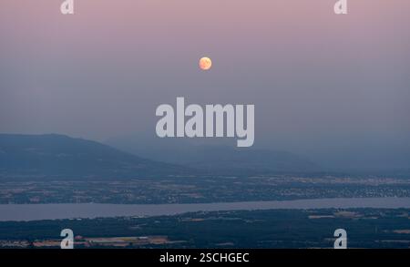 Eine ruhige Szene mit Vollmond, der über dem Lake Leman aufsteigt und einen Glanz über die umliegende Landschaft wirft und Chillon Castle in der Ferne hervorhebt. Stockfoto