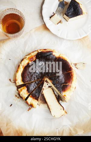 Blick von oben auf ein minimalistisches Foto mit einem frisch gebackenen San Sebastian Käsekuchen, serviert auf Pergamentpapier und einem Honigglas. Stockfoto