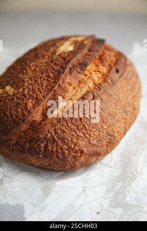 Eine Nahaufnahme eines frisch gebackenen Sauerteigbrotes mit einer wunderschön strukturierten Kruste, präsentiert auf zerknittertem weißem Papier. Stockfoto