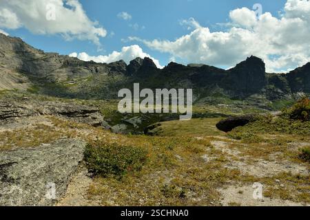 Der Rand einer Klippe mit geschichteten Steinen mit Blick auf die malerischen Bergketten von spitzer ungewöhnlicher Form. Naturpark Ergaki, Region Krasnojarsk, Stockfoto