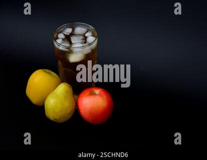Apfel- und Birnensaft in einem hohen Glas mit Eis auf schwarzem Hintergrund, neben Reifen Früchten. Nahaufnahme. Stockfoto