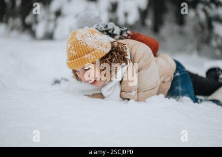 Lächelnde Frau, die einen verspielten Moment in der schneebedeckten Natur genießt und ein gemütliches Winteroutfit trägt Stockfoto
