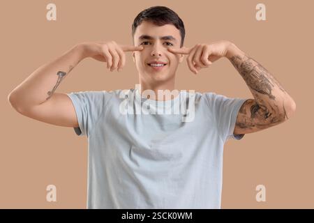Junger Mann, der Gesichtsaufbauübung auf beigefarbenem Hintergrund macht Stockfoto