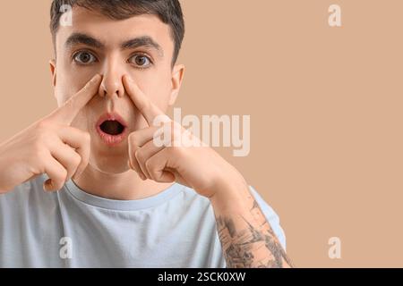 Junger Mann, der Gesichtsaufbauübung auf beigefarbenem Hintergrund macht Stockfoto