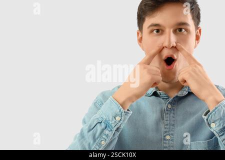 Junger Mann, der Gesichtsbauübung auf hellem Hintergrund macht Stockfoto