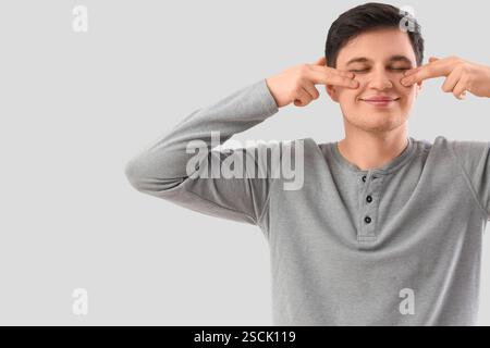 Junger Mann, der Gesichtsbauübung auf hellem Hintergrund macht Stockfoto