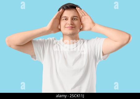 Junger Mann, der Gesichtsaufbauübung auf blauem Hintergrund macht Stockfoto