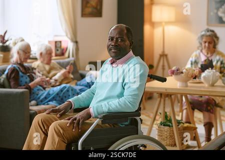 Porträt eines älteren afroamerikanischen Mannes mit Behinderung, der im Wohnzimmer eines Pflegeheims für ein Foto posiert Stockfoto