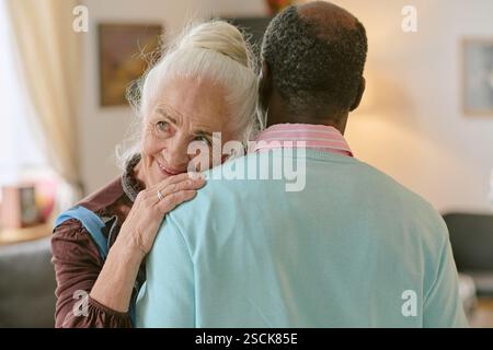Mittlere Nahaufnahme einer älteren, eleganten Frau, die während des langsamen Tanzes den Kopf auf eine nicht erkennbare afroamerikanische Schulter legt Stockfoto