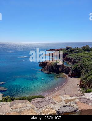 Malerische Mittelmeerküste mit kristallklarem Wasser Und atemberaubendem Blick auf eine Mittelmeerküste mit türkisfarbenem Wasser und zerklüfteten roten Felsen. Stockfoto