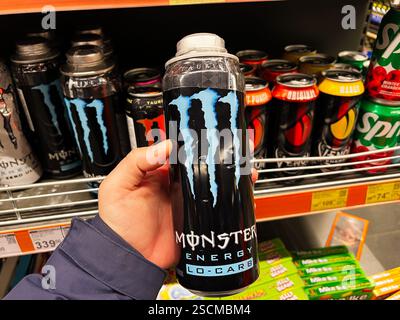 Kiew, Ukraine - 04. Februar 2025: Nahaufnahme einer Hand, die ein beliebtes Energiegetränk von Monster in einem Regal in einem Geschäft hält. Stockfoto
