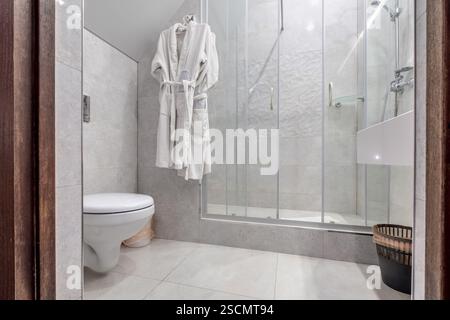 Helles und elegantes Bad mit verglaster Dusche, wandmontierter Toilette und Fliesen in Marmoroptik für einen eleganten, luxuriösen Look. Stockfoto