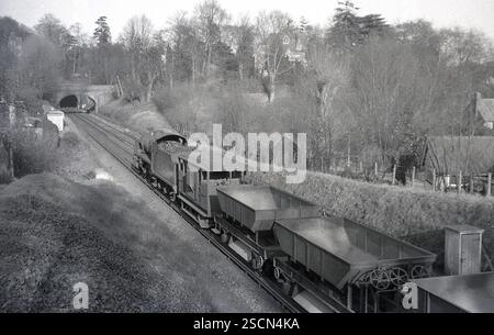 1950er Jahre, historische Dampflokomotive auf Landgleis, die Güterwagen zieht, kurz vor dem Tunnel, England, Großbritannien. Stockfoto