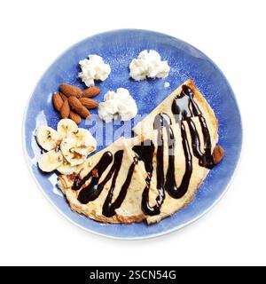 Köstliche Crepes mit Schokoladensauce, Banane, Mandeln und Schlagsahne isoliert auf weiß, Blick von oben Stockfoto