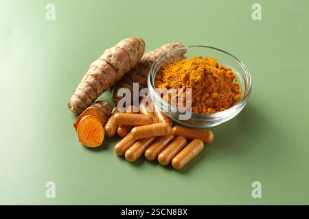 Kurkumapulver in Schüssel, Wurzeln und Kapseln auf grünem Hintergrund Stockfoto