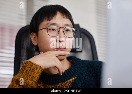 Porträt eines asiatischen Mannes mit Brille und aufliegendem Kinn, der vor einem Computer sitzt und tief in Gedanken erscheint Stockfoto