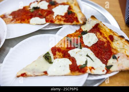 Pizza mit Käse und Basilikum darauf. Es ist auf einer weißen Platte. Auf dem Teller sind zwei Pizzabäcke Stockfoto