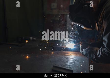 Schweißer in Schutzausrüstung, der mit Metall arbeitet, indem er eine Schweißmaschine verwendet, die helle Funken, Blitze und Dämpfe erzeugt. Stockfoto
