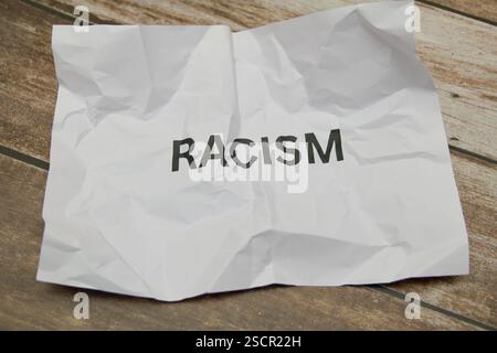 Ein zerknittertes Blatt Papier zeigt das Wort Rassismus in fetten Buchstaben auf einem strukturierten Holzhintergrund. Stockfoto