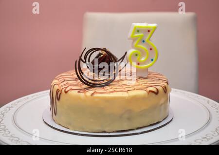 Geburtstagskuchen mit Kerze Nummer drei zum Feiern von 3 Jahren oder 3 Jahrzehnten des Lebens - auf einem Tisch Stockfoto