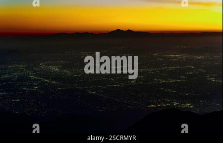 Faszinierender Blick auf das San Bernardino Valley in der Abenddämmerung von Rimforest, Kalifornien, mit einer Mischung aus lebhaften Farben bei Sonnenuntergang und glitzernden Lichtern der Stadt. Stockfoto