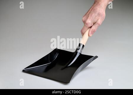 Neuer und sauberer schwarzer Metallstaubbehälter, der von Mann Hand in Studio-Licht auf weißem Hintergrund gehalten wird Stockfoto