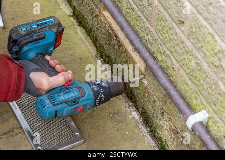 Ein Mann (Mann, Arbeiter, Handwerker), der mit einem tragbaren Bohrer Löcher in Ziegelsteine bohrt. Die Bohrungen dienen zum Anschrauben einer Abdeckung aus Luftziegeln. Stockfoto