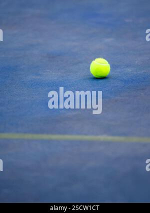 Einzelner grüner Tennisball, der auf einem Blue Court sitzt Stockfoto