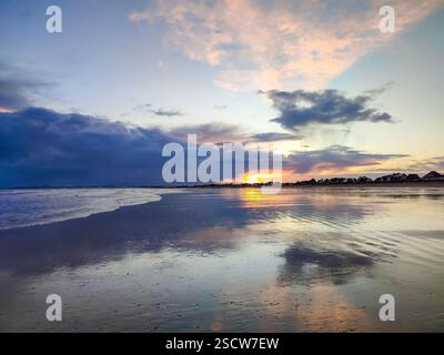 Die Wellen schlagen sanft gegen die Küste, während die Sonne untergeht, und strahlen leuchtende Farben in den Himmel. Stockfoto
