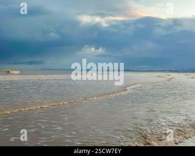Sanfte Wellen Rollen am Strand, während sich am Nachmittag dunkle Wolken über dem Horizont sammeln. Stockfoto