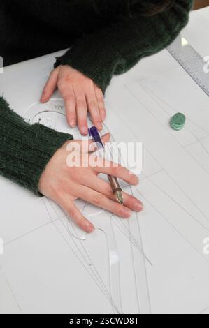 Eine junge Frau zeichnet Kurven mit einer Plastikpistole und einem mechanischen Bleistift auf einem weißen Blatt Papier. Neben ihren Händen befindet sich ein Herrscher und ein Radierer. Stockfoto