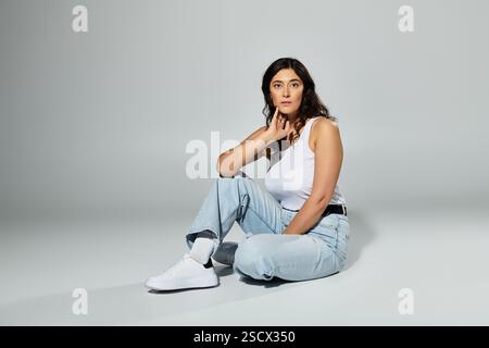 Damen in Übergröße zeigen Selbstvertrauen in stilvollem weißem Tanktop und lässiger Jeans. Stockfoto