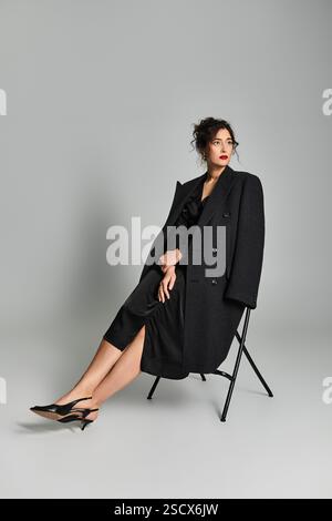 Elegante Brünette posiert anmutig in stilvoller schwarzer Kleidung vor grauem Hintergrund. Stockfoto