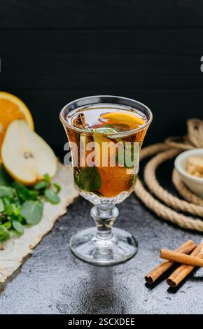 Aromatischer Kräutertee mit Zitrusfrüchten, Zimt und Minze in einem Glas, auf einem dunklen rustikalen Hintergrund Stockfoto