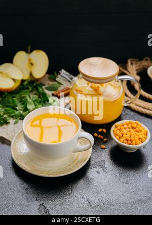 Sanddorntee mit Apfel und Minze in Glas-Teekanne auf rustikalem Hintergrund, perfekt für Wellness Stockfoto